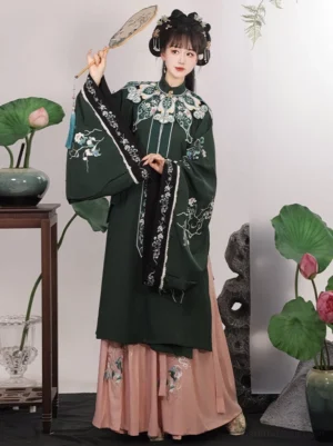 Front view of a blue green Ming Dynasty Hanfu outfit with floral embroidered robe, pink pleated Mamian skirt, decorative cloud collar, lotus plants, and Chinese garden studio decor
