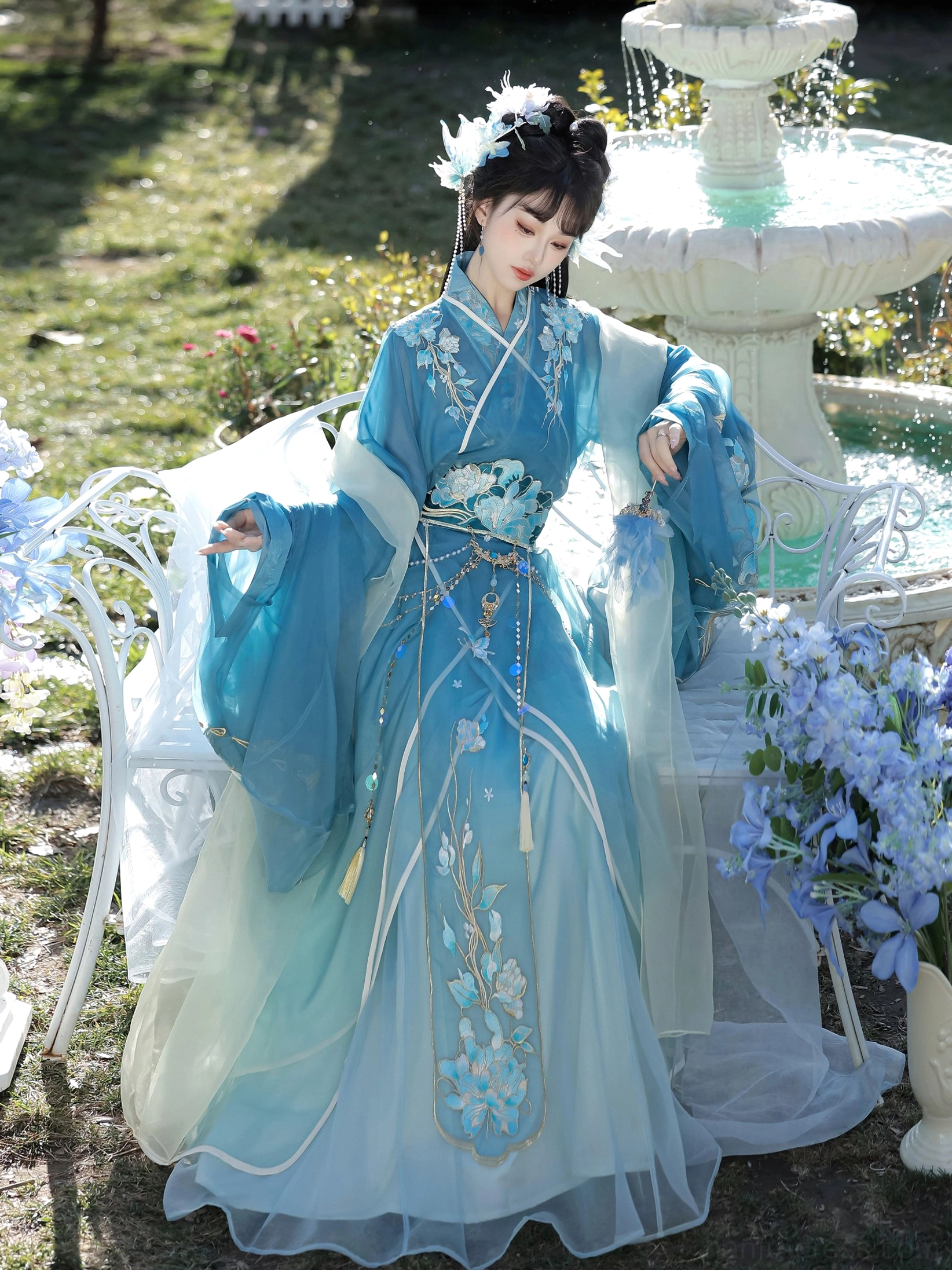 Blue gradient Han Dynasty Hanfu straight hem robe shown in a three-quarter front full-body garden portrait with floral embroidery, sheer layered fabric, and decorative waist tassels