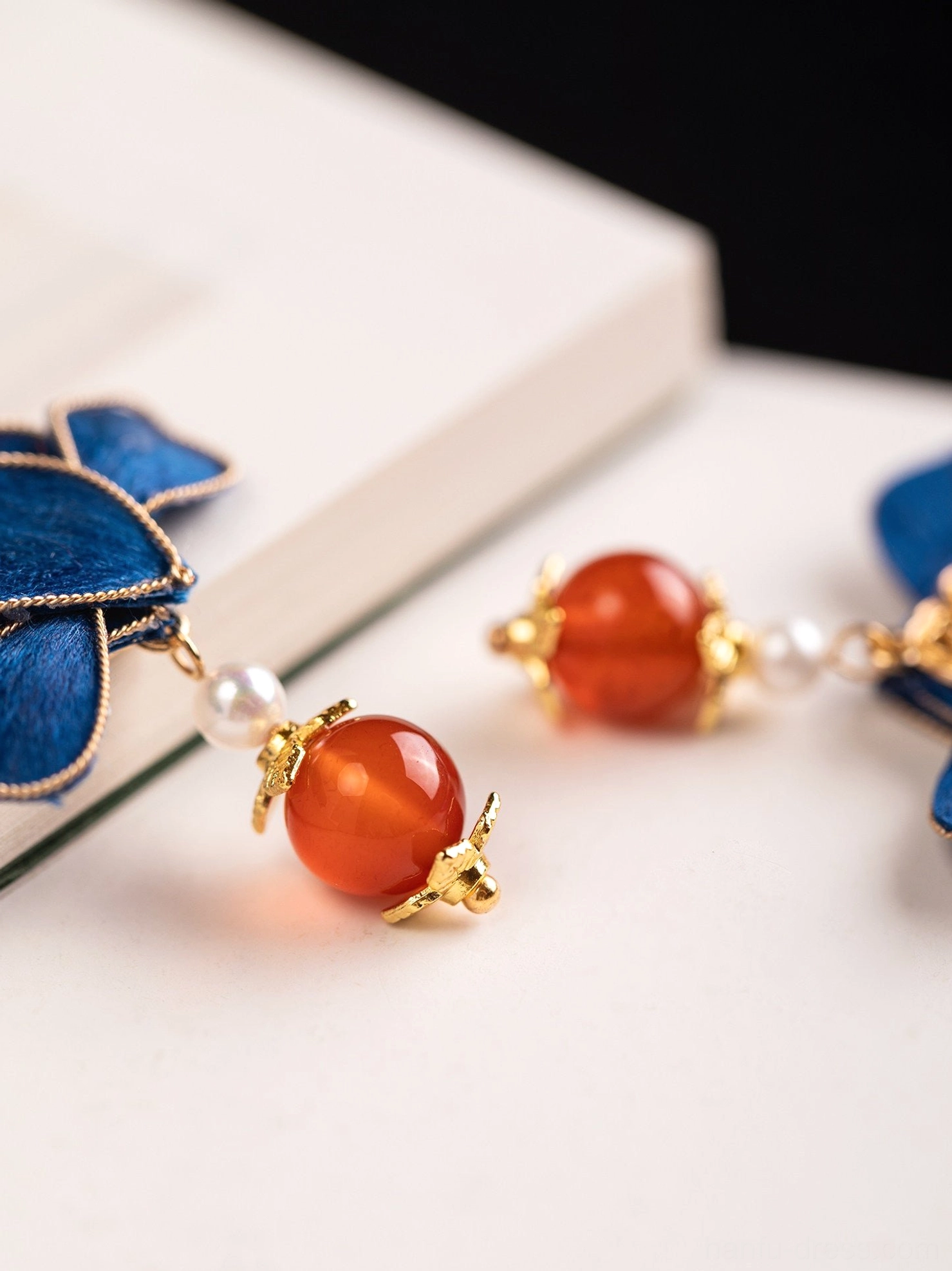 Close-up side view of blue lotus Chinese drop earrings showing pearl accent, red agate-style bead and gold filigree caps