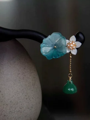Close-up of a traditional Chinese lotus hair stick with black curved wooden shaft, translucent blue lotus flower, white blossom with gold center, and green lotus seed pod pendant