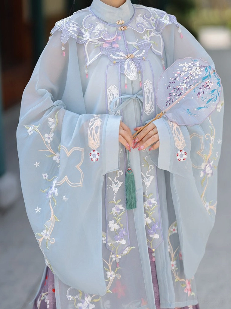 Close-up of light cyan Ming-style Hanfu blouse with cloud and floral embroidery, stand collar, front placket, and green tassel pendant