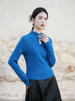 Blue modern Hanfu knitted top shown from a three-quarter left view with a stand collar, keyhole neckline, decorative Chinese frog button, long sleeves, and a black embroidered pleated mamian skirt