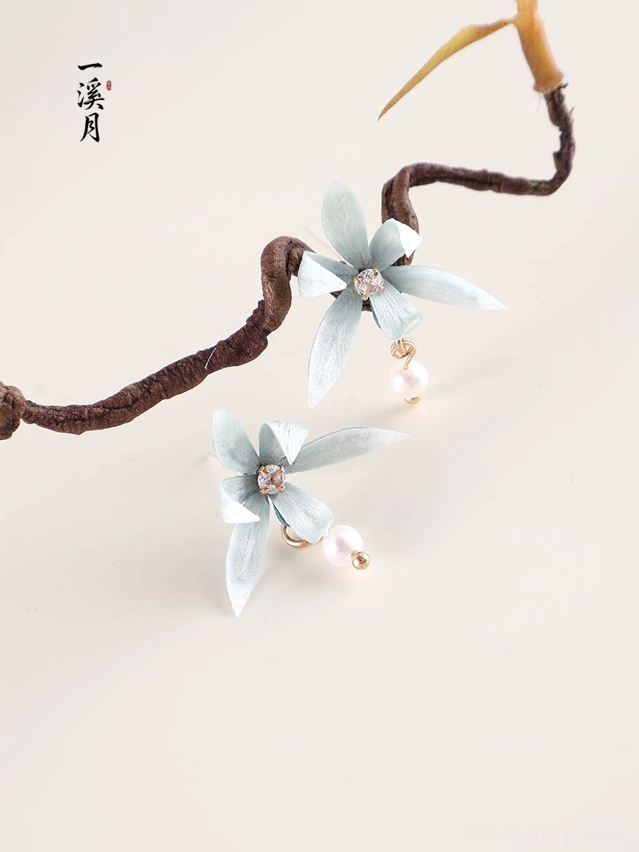 Elegant blue orchid Chinese earrings with pearl drop charms and gold tone metal details beside a curved dried tree branch