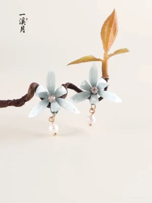 Blue orchid pearl drop Chinese earrings flat lay with delicate cyan flower petals, rhinestone centers, gold tone hardware and dried branches