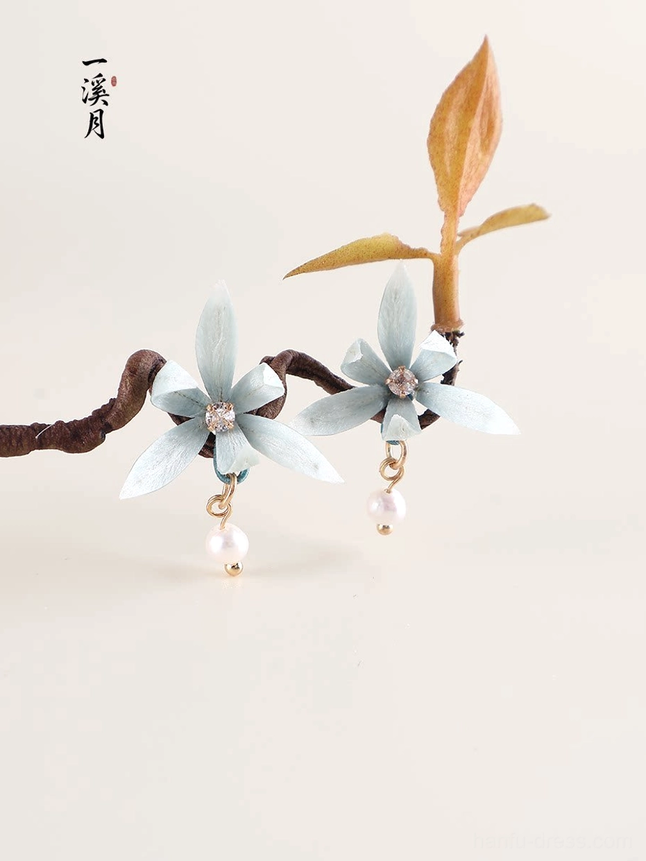 Blue orchid pearl drop Chinese earrings flat lay with delicate cyan flower petals, rhinestone centers, gold tone hardware and dried branches