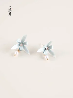 Pair of blue orchid stud earrings with pearl drops, gold tone fittings and sparkling flower centers on a neutral background