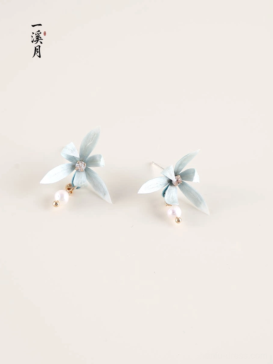 Pair of blue orchid stud earrings with pearl drops, gold tone fittings and sparkling flower centers on a neutral background