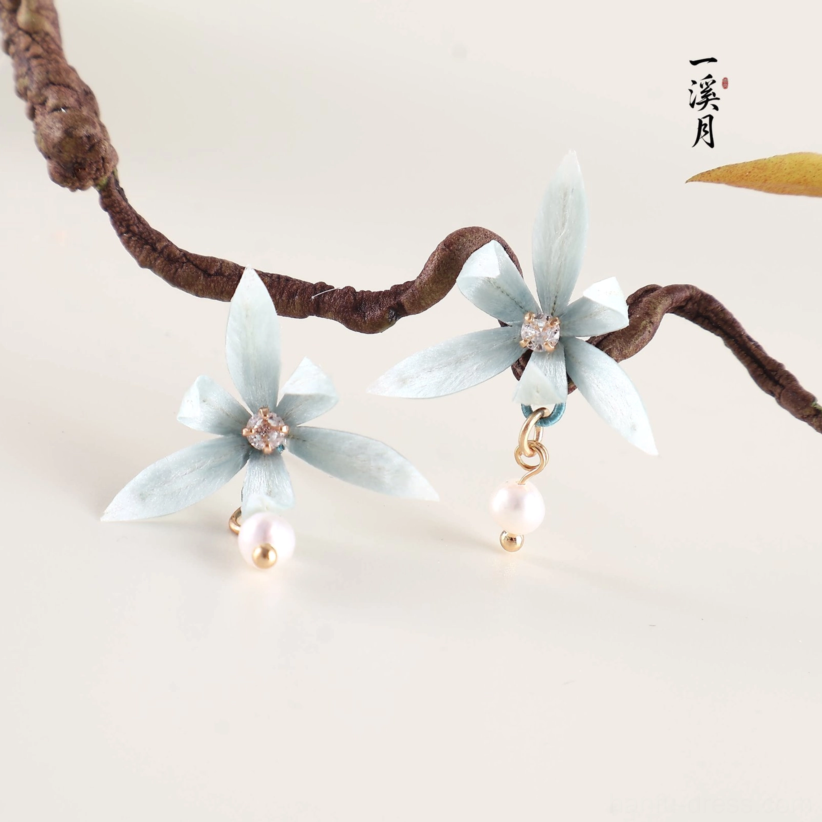 Close-up of blue orchid stud earrings showing textured cyan petals, sparkling centers, gold jump rings and pearl drop details