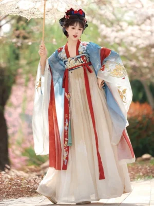 Front full-body view of a blue and cream Tang Dynasty Qixiong Ruqun Hanfu outfit with embroidered wide sleeves, red sashes, pleated skirt, and traditional hair ornaments in a spring flower garden