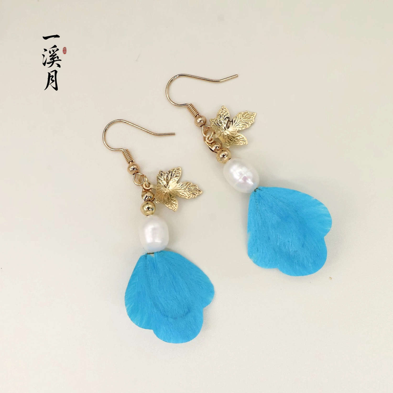 Pair of blue velvet flower maple leaf Chinese drop earrings with gold-tone hooks and pearl-like bead accents in full flat lay view
