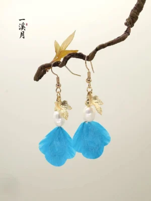 Blue velvet flower Chinese drop earrings with gold maple leaf charms and pearl-like bead accents displayed on a natural branch