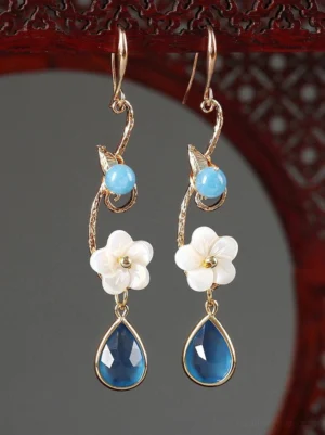 Close-up of blue and white floral water lily Cheongsam earrings displayed on a traditional red carved wooden jewelry stand