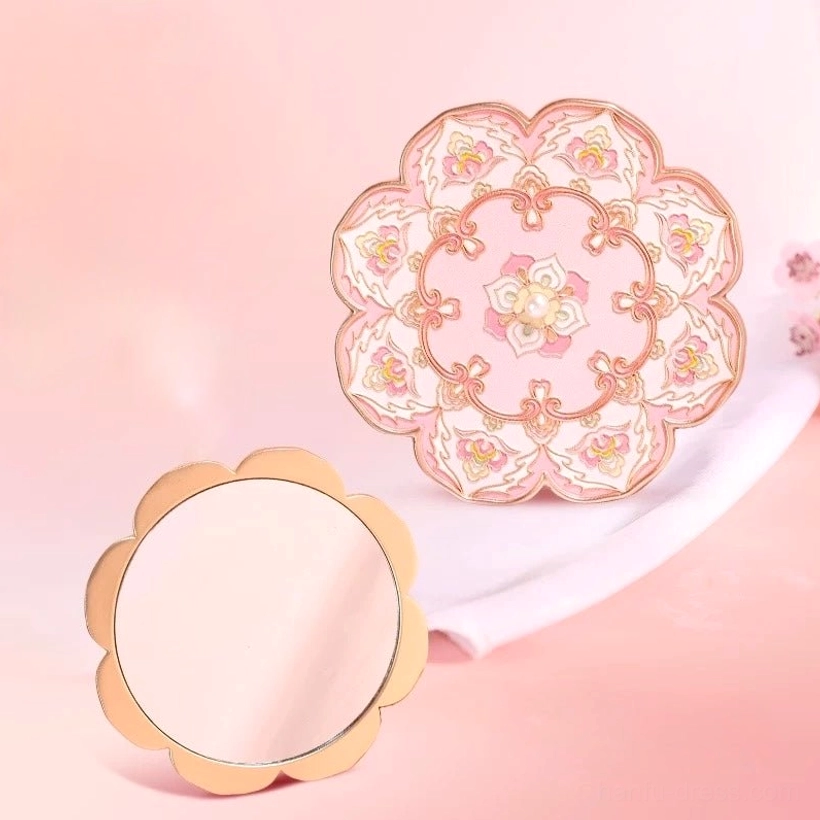 Blushing lotus blossom Chinese pocket mirror shown open and closed on a warm pink background, featuring a reflective mirror face and ornate pink floral back cover with rose gold-tone scalloped frame