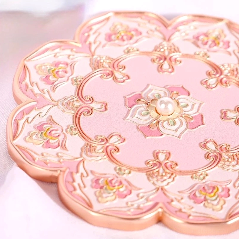 Macro close-up of blushing lotus blossom Chinese pocket mirror back cover with raised oriental floral scrollwork, pearl-like centre accent, pink finish, and rose gold-tone border