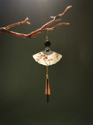 Single brown bamboo fan-shaped Chinese earring hanging from a tree branch, featuring a black bead, gold hook, and long tapered metal tassel