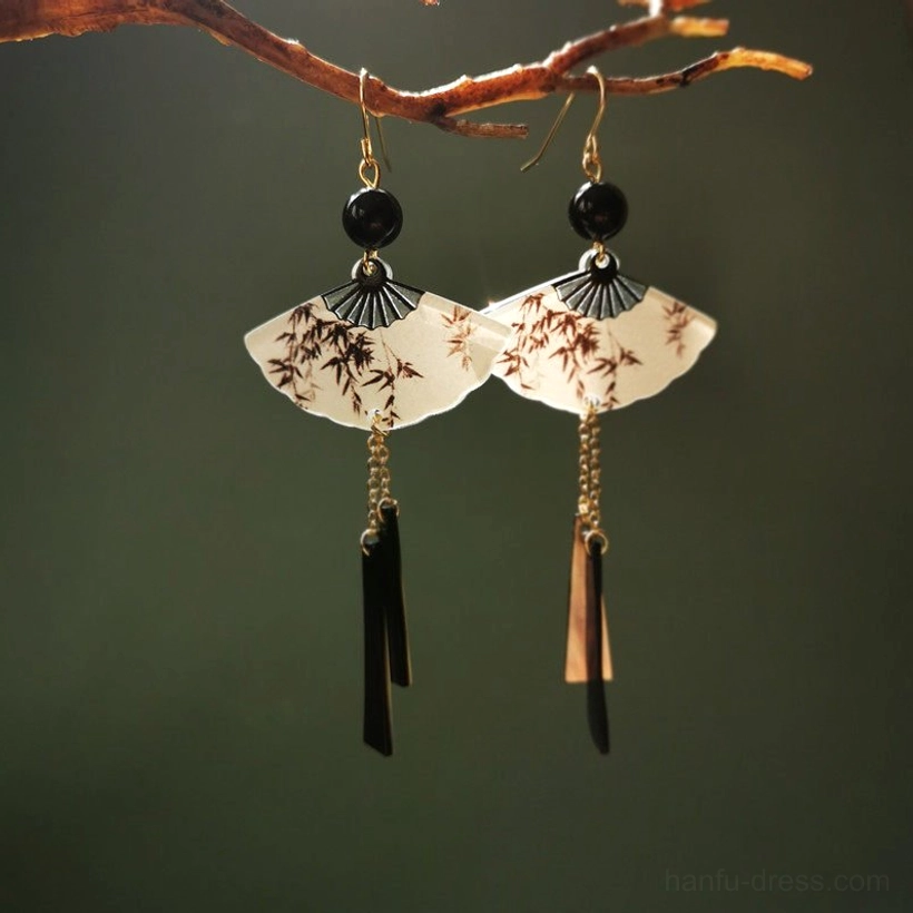 Matching brown bamboo fan Chinese earrings hanging from a bare branch with black beads, gold ear hooks, and dark metal strip tassels