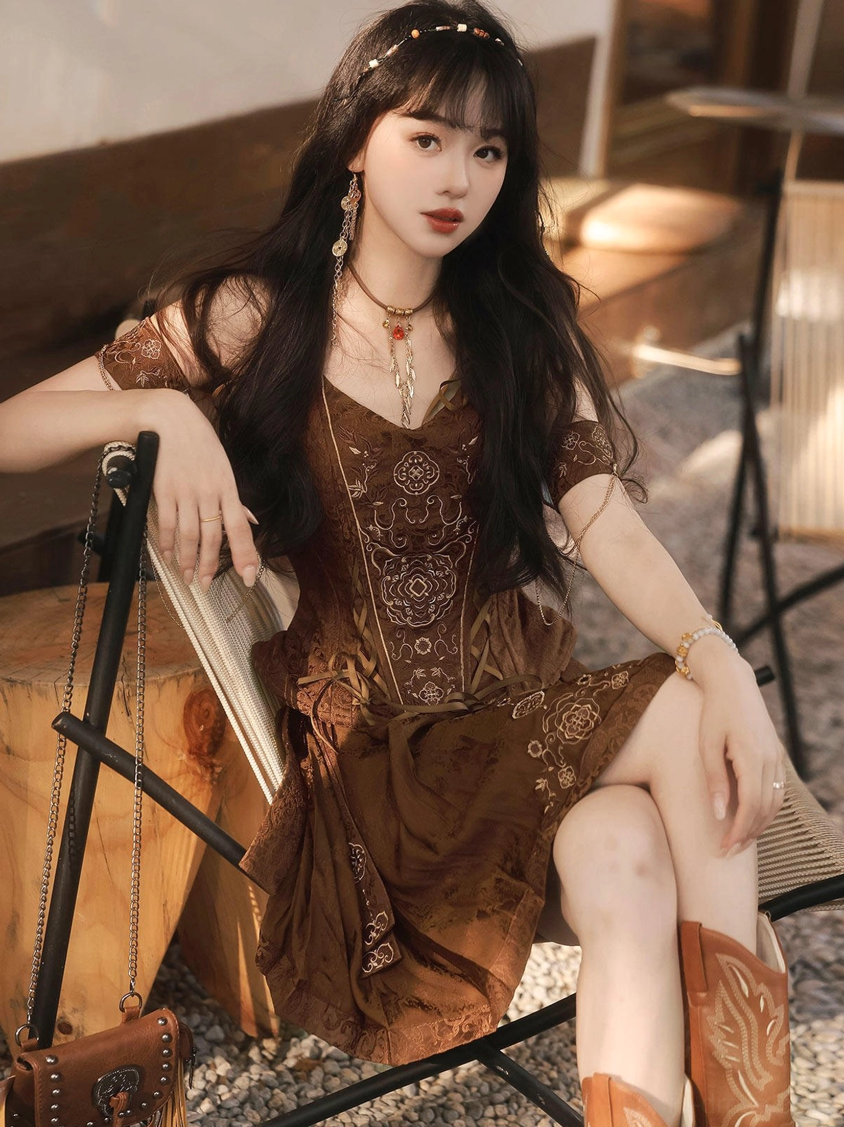Model sitting in a brown Ming-style Hanfu outfit with embroidered bustier, short horse-face skirt, layered necklaces, and boots