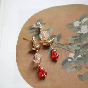 Budding Birds Chinese Hanfu dangle earrings with gold bird-shaped studs, clear crystal accents, and red bellflower pendant charms displayed on a classical Chinese flower-and-bird painting background