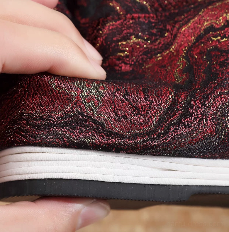 Close-up detail of burgundy and black woven Hanfu boot fabric with shimmering gold thread patterns, layered cloth midsole, and textured black rubber outsole