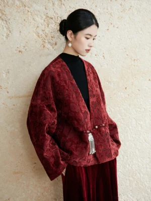 Burgundy festive Hanfu coat shown from a left rear full-body angle with dark floral jacquard fabric, loose drop-shoulder silhouette, batwing sleeves, and silver tassel fastener