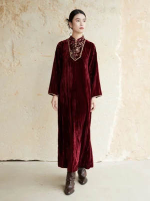 Full front view of a burgundy embroidered velvet Chinese New Year Hanfu dress with stand collar, loose long sleeves, gold trim, and floor-length straight silhouette