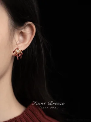 Close-up of burgundy firework stud earring worn on ear, gold-tone Chinese festival jewelry with crystal accent