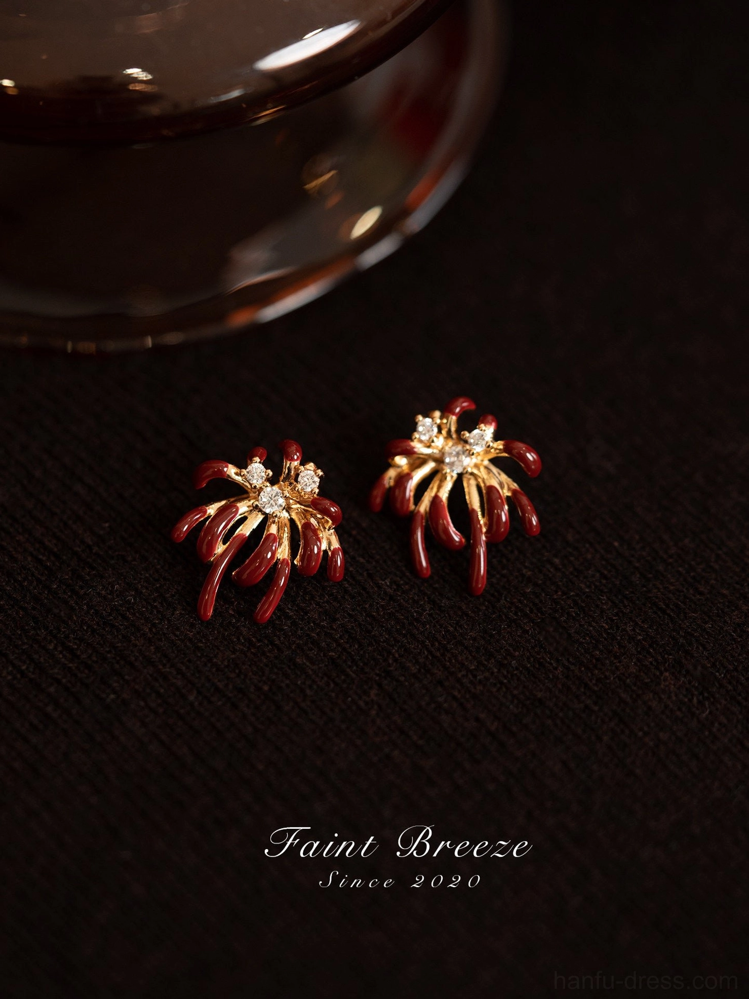 Pair of burgundy and gold firework Chinese stud earrings with sparkling center crystals on dark fabric