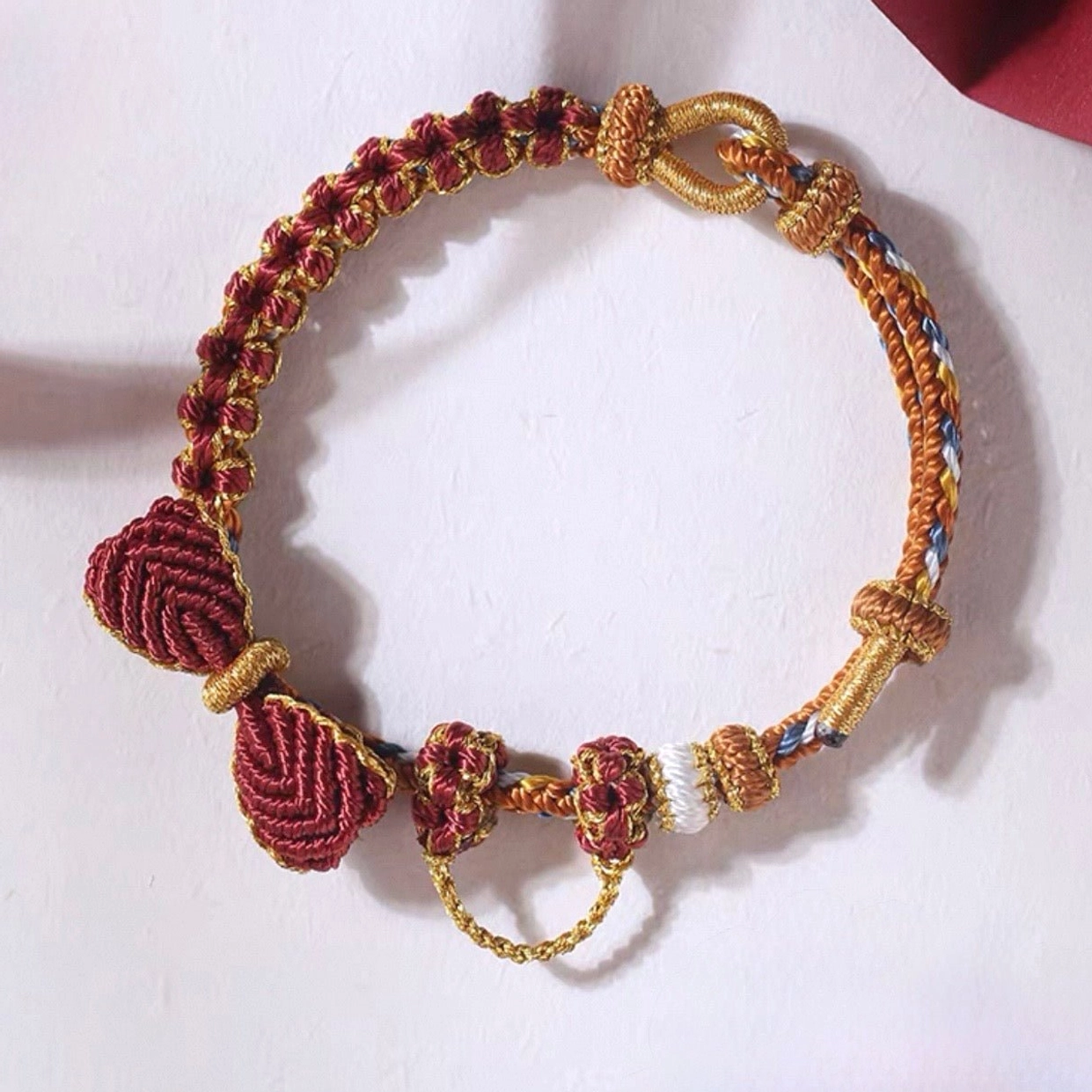 Burgundy handwoven Chinese knot bow bracelet with floral knot ornaments, gold-tone accents, and braided cord on white background