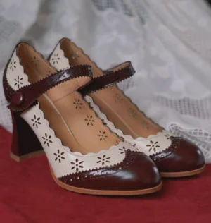 Three-quarter side view of burgundy and ivory Chinese traditional Mary Jane shoes with floral openwork, scalloped edges, button-fastened ankle straps, and chunky low block heels