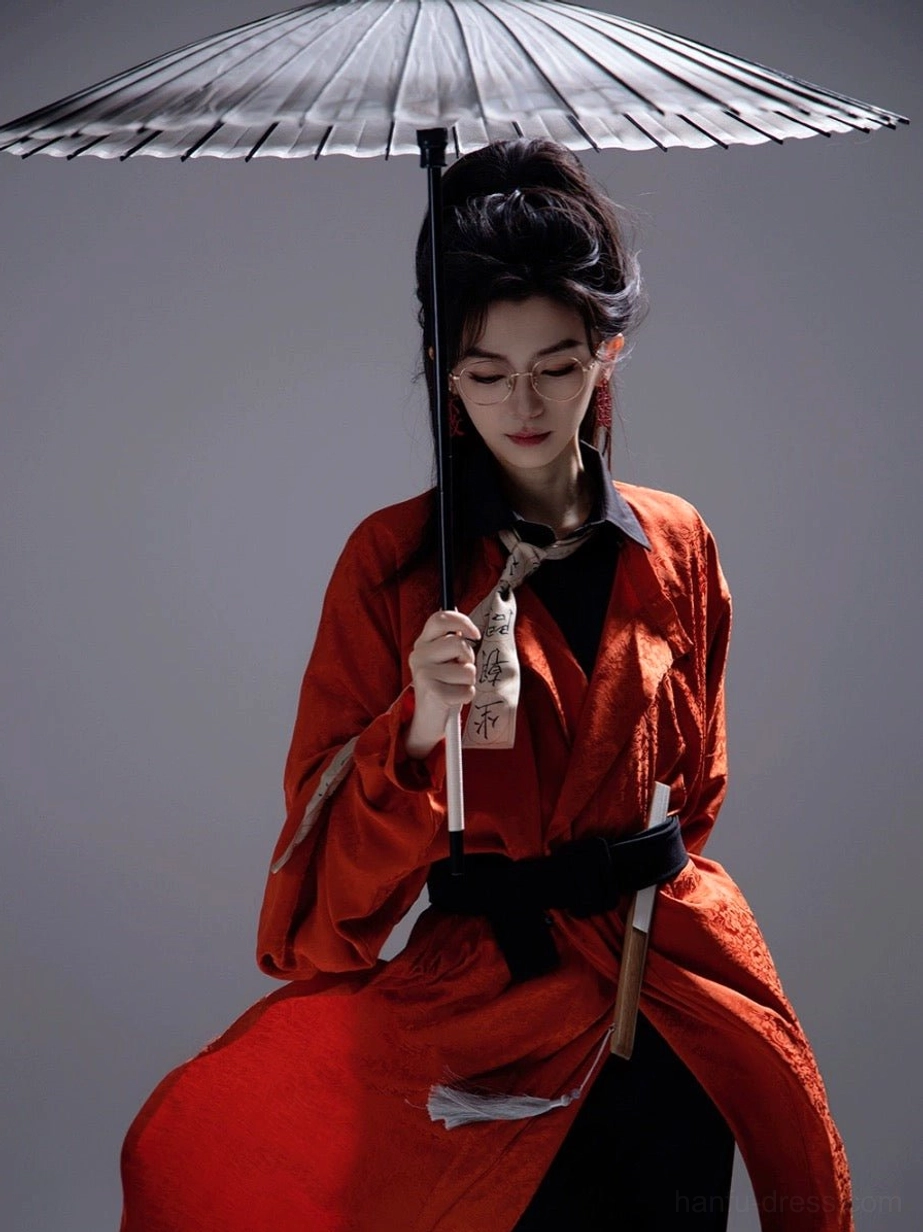 Front three quarter view of burnt orange Tang style round collar Hanfu robe styled with black belt and traditional oil paper umbrella