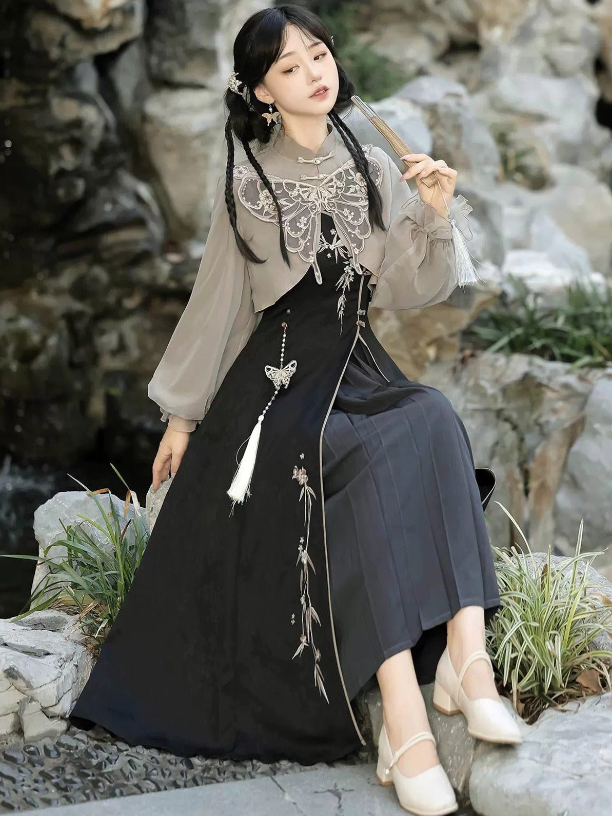 Low-angle seated view of the Butterfly Ash Chinese-style summer sundress showing the two-tone grey and black modern Hanfu silhouette, delicate embroidery, cloud collar, and traditional tassel accessories
