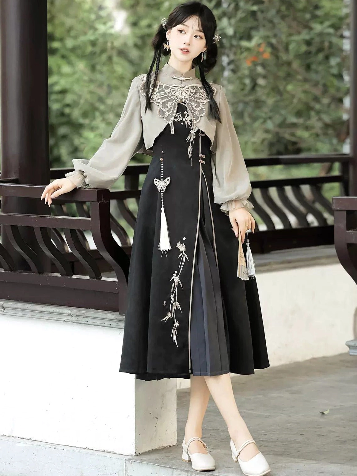 Side view of a woman wearing a modern Hanfu midi dress with elegant grey lantern sleeves, black embroidered skirt, butterfly-inspired collar, and tassel details beside a traditional Chinese pavilion
