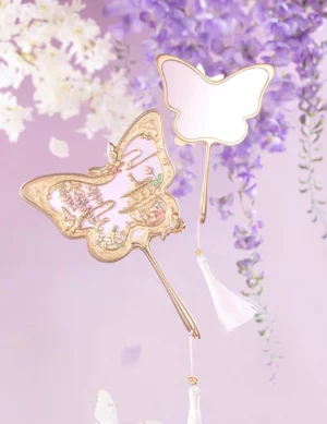 Butterfly-shaped Chinese hand mirror with rose-gold carved pavilion frame, pastel floral details, white tassel, and wisteria-inspired decorative setting