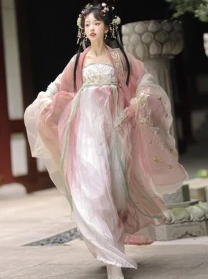 Butterfly Dream Tang Dynasty style Hanfu dress in a pink and ivory chiffon gradient with embroidered floral sleeves, light green sash, and flowing Heziqun skirt worn in a classical Chinese courtyard