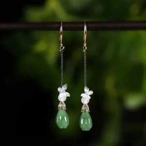 Butterfly jade Chinese dangle earrings with white butterfly charms green chain details and jade-green teardrop pendants on black display stand