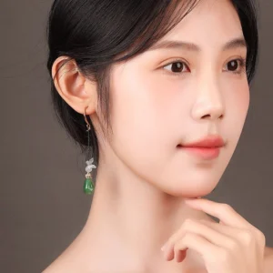 Model wearing butterfly jade Chinese dangle earring with white butterfly charm and long jade-green teardrop pendant