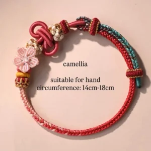 Camellia themed handwoven Chinese knot bracelet in wine red lake blue and light pink with pearl clusters beaded flower ornament and traditional Chinese disc knot on a light pink background