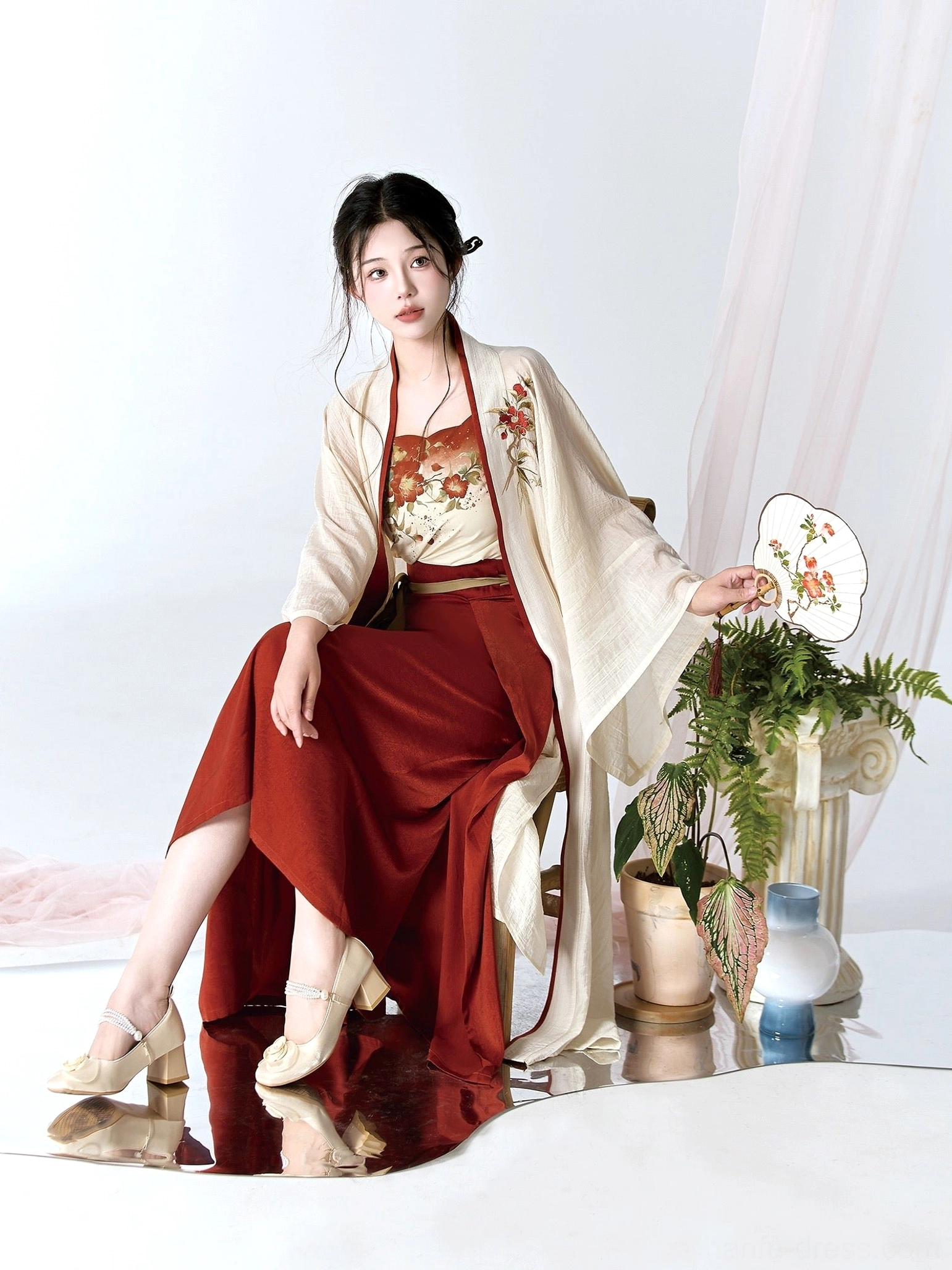 Side sitting view of a woman wearing a camellia Hanfu outfit with textured cream cardigan, floral embroidery, and burgundy skirt