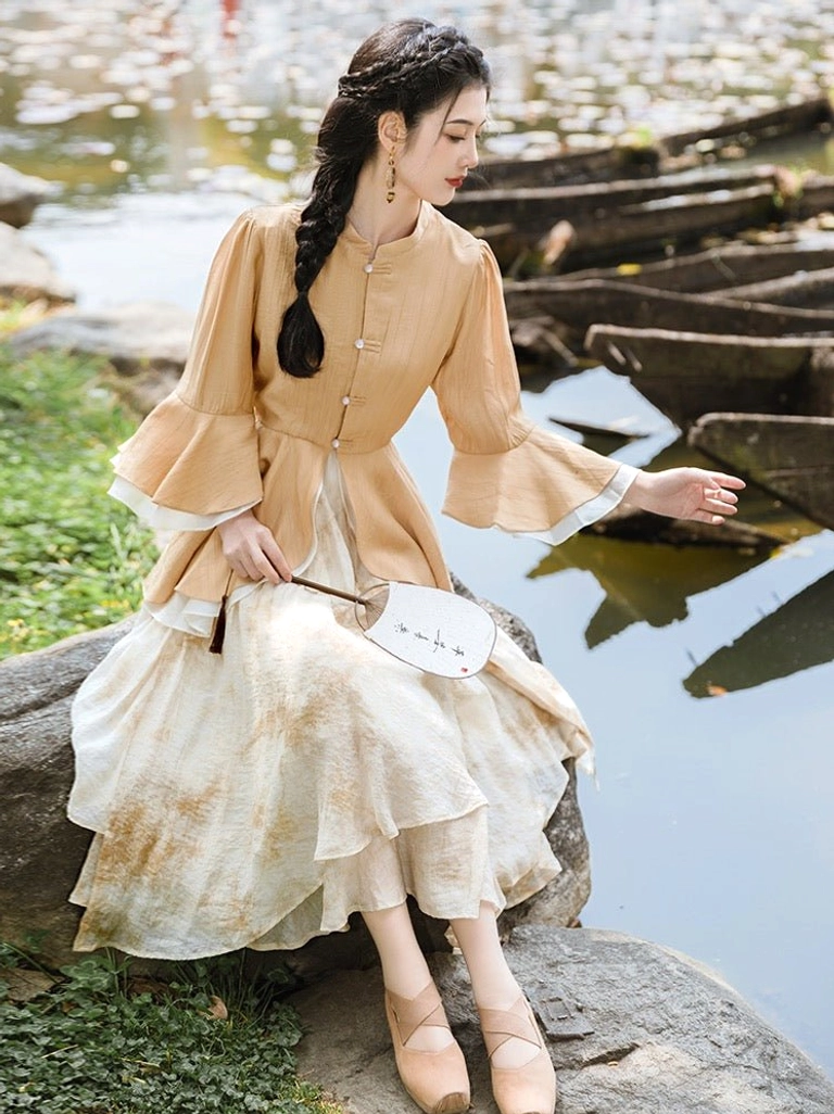Canary yellow modern Ming style Hanfu two-piece outfit with ruffle sleeve stand collar top and beige gradient midi skirt worn beside a lakeside garden
