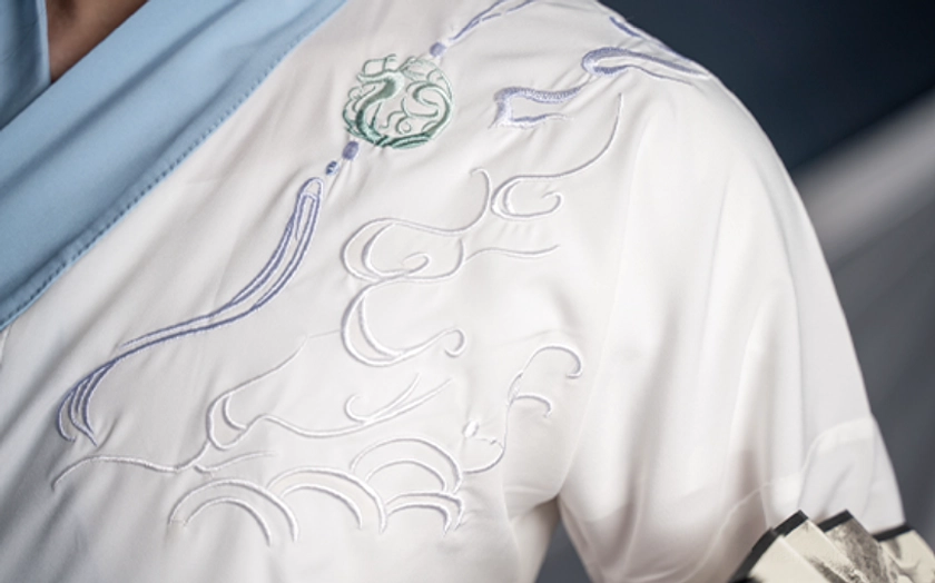 Close up of white cross collar inner top with light blue trim, cloud embroidery and tassel detail from the Carefree wuxia hanfu set