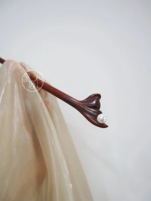Carved flower pearl Chinese hair stick in dark reddish-brown wood displayed on champagne silk Hanfu fabric