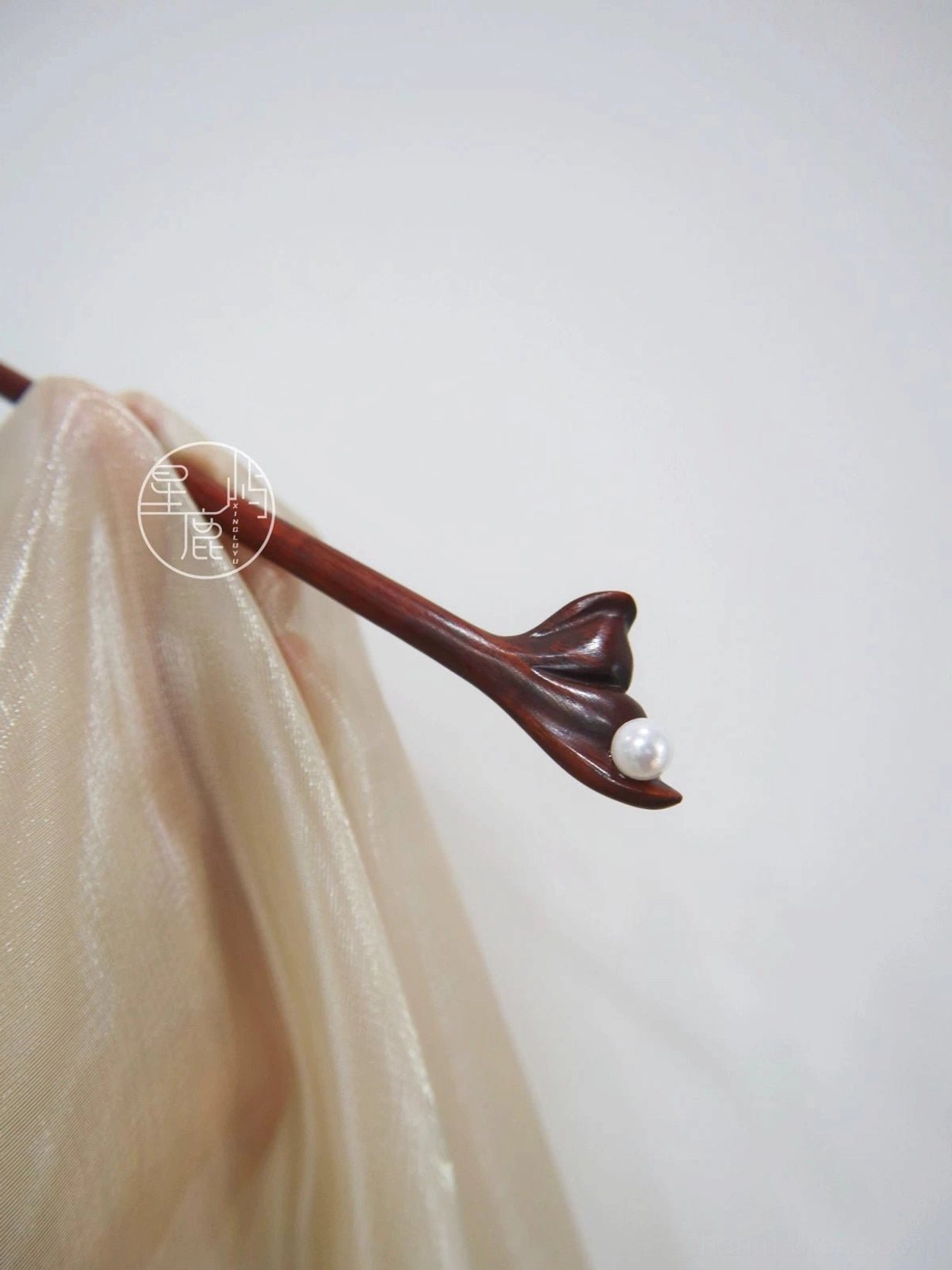 Carved flower pearl Chinese hair stick in dark reddish-brown wood displayed on champagne silk Hanfu fabric