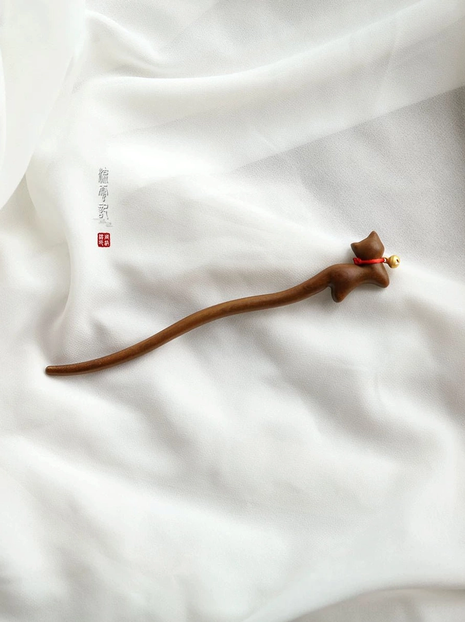 Full-length cat-shaped Chinese hair stick displayed on white linen, showing the long wooden shaft, lying cat ornament, red collar, and golden bell