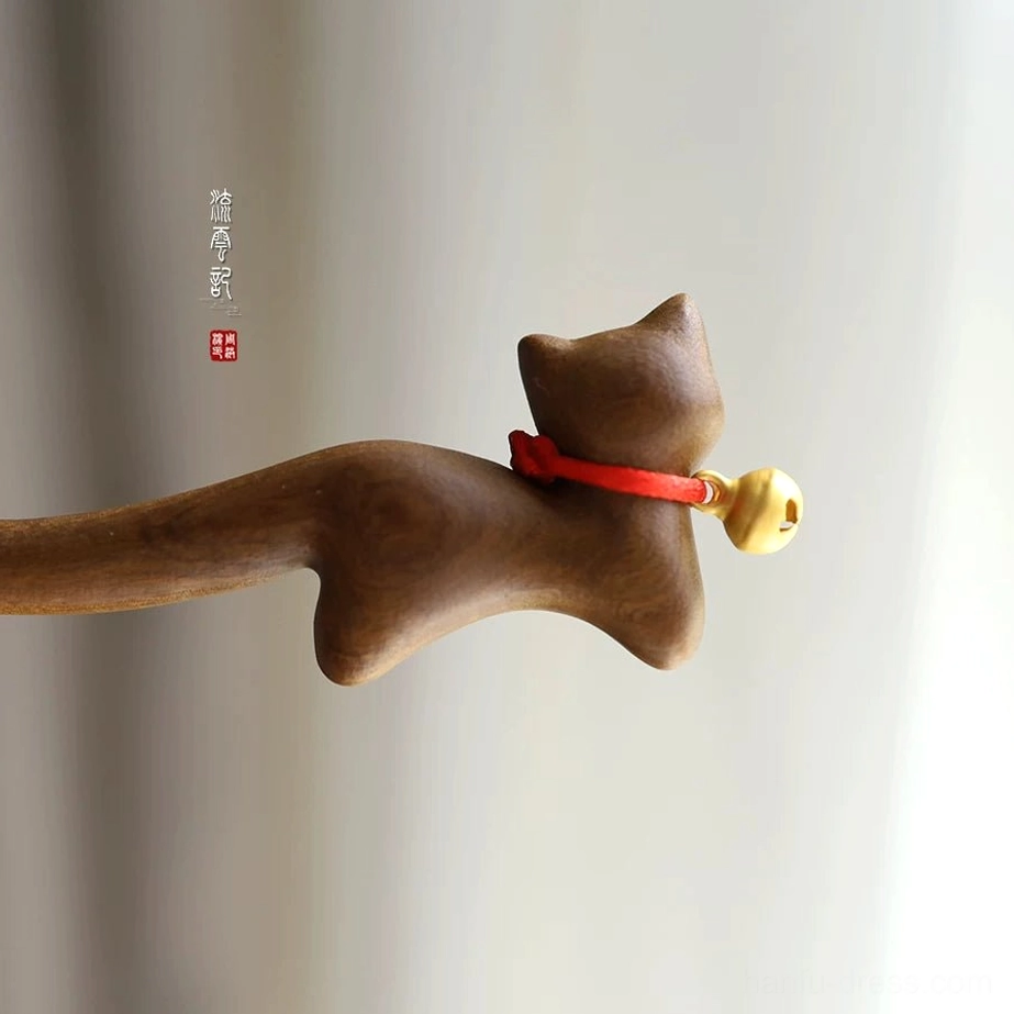 Side close-up of a cat-shaped wooden Chinese hair stick with smooth brown wood grain, red collar, and brass-toned hanging bell
