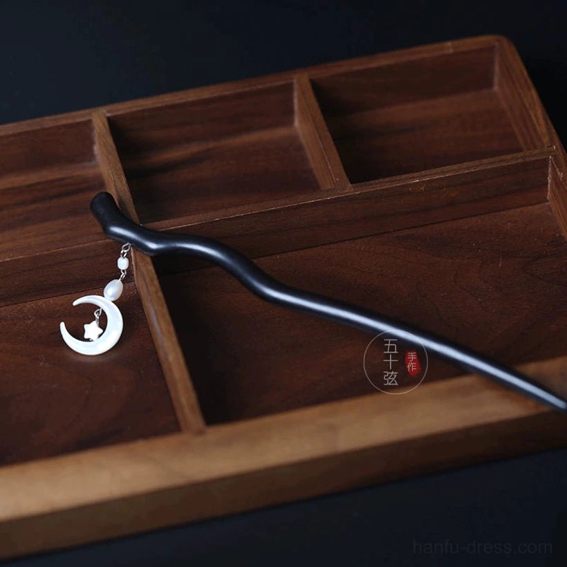 Top view of celestial Hanfu hair stick featuring a wavy dark wooden shaft, crescent moon star charm, and pearl pendant on wooden tray