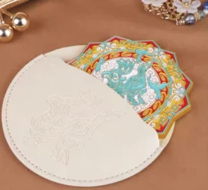 Celestial qilin Chinese pocket mirror displayed with its matching beige leather storage pouch featuring an embossed qilin design and decorative jewellery accents