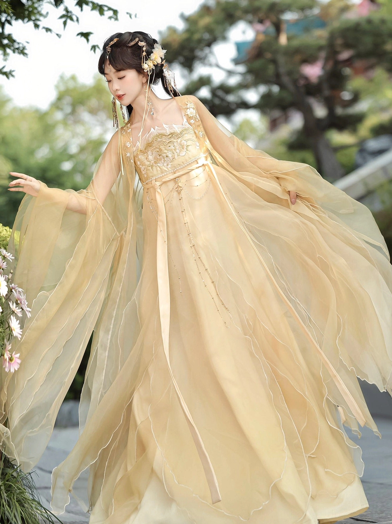 Champagne gold Tang Dynasty Qixiong Ruqun hanfu shown in a flowing side view outdoors with sheer organza fabric, embroidered chest panel, soft ruffled sleeve edges, and layered skirt movement