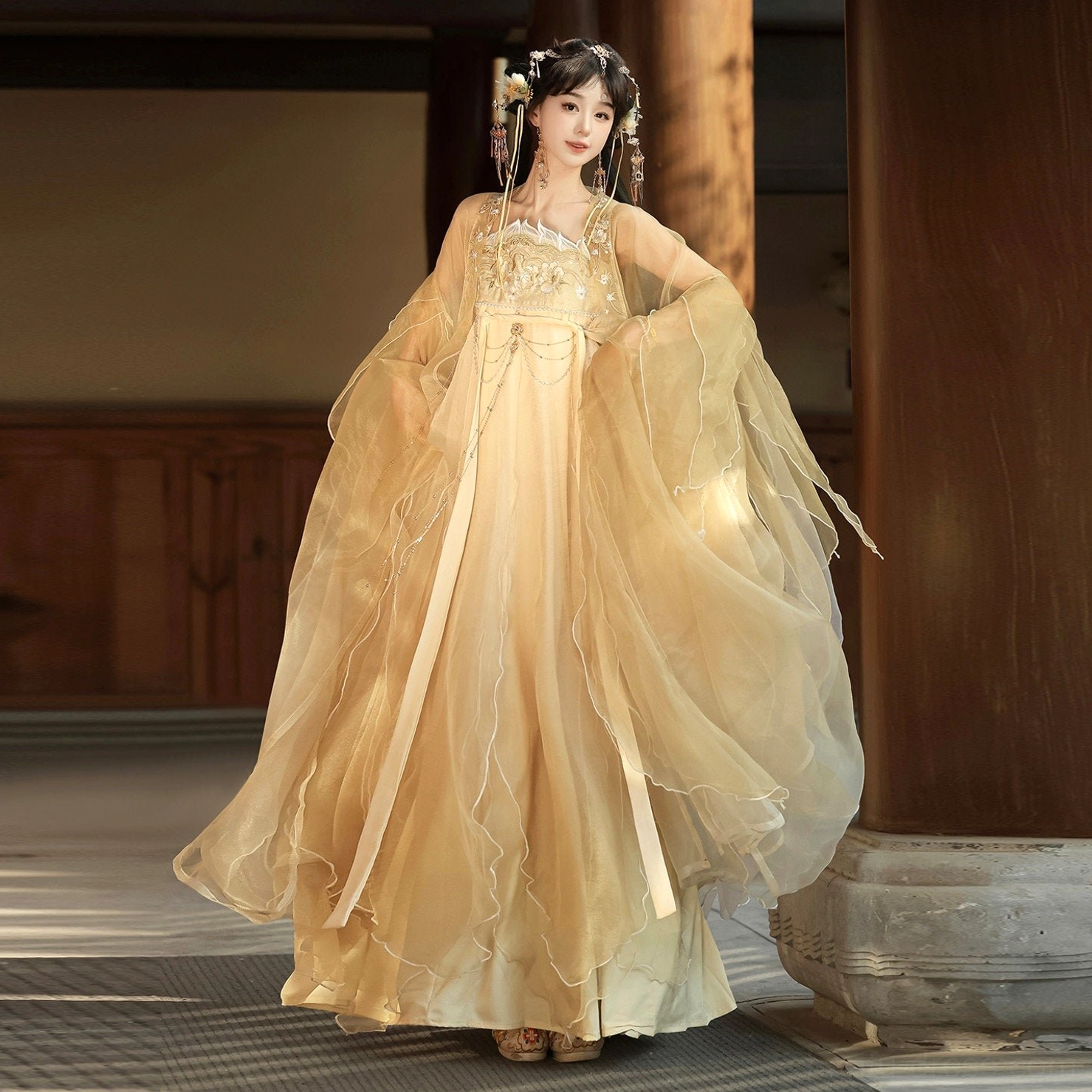 Champagne gold Tang-style Qixiong Ruqun hanfu full set shown from a back three-quarter view with floor-length organza skirt, wide ruffled sleeves, waist sash, and decorative waist chain in a traditional courtyard