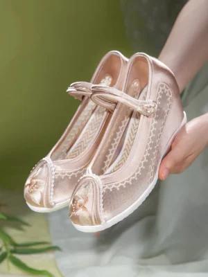Close-up of champagne pink traditional Chinese Hanfu shoes showing floral embroidery, delicate lace trim, white rubber outsole, wedge heel, and zigzag patterned insole