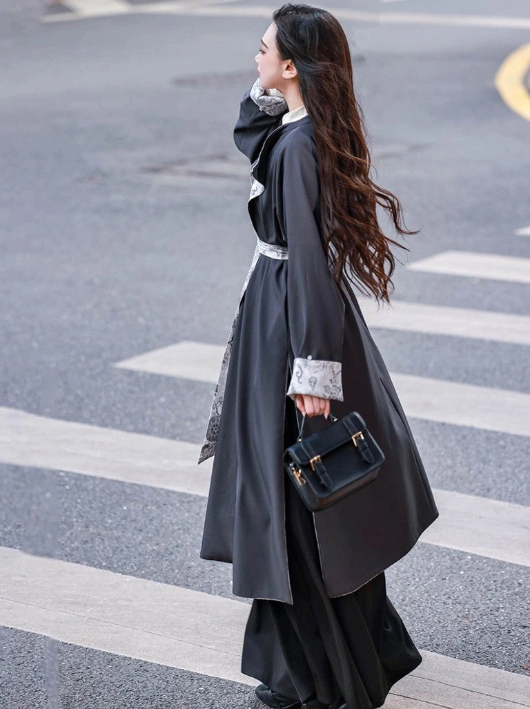 Back three-quarter view of a charcoal gray reversible Hanfu robe with flowing long hem matching waist sash and modern leather handbag styling